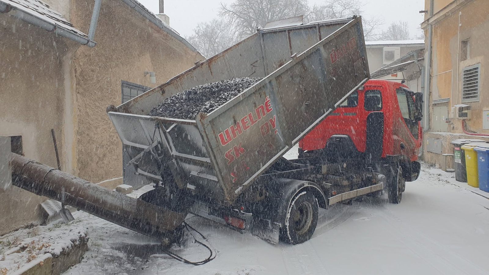 Vůz Uhelné sklady Sadská sype uhlí do pásového dopravníku u domu za sněžení